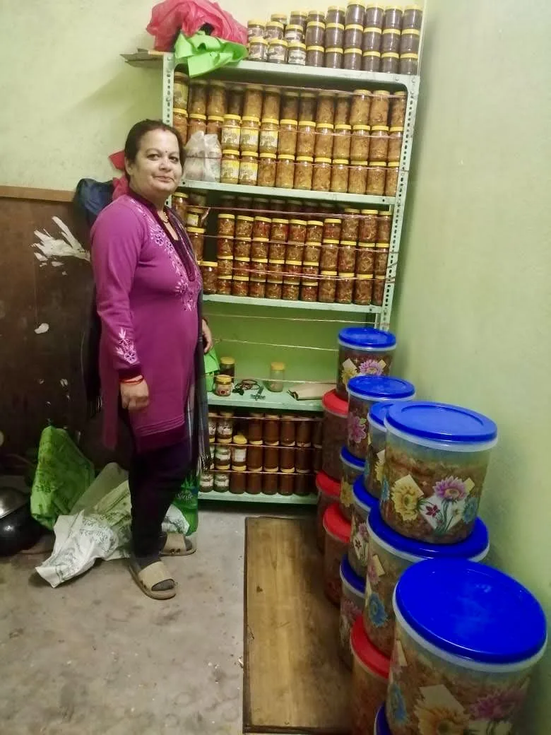 Saraswati Adhikari standing beside shelves of the first My Pickle House jars in the family's original production room