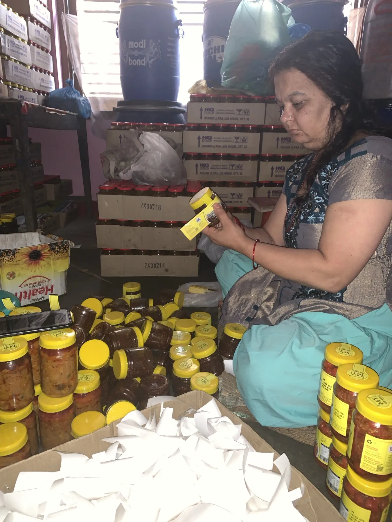 Saraswati Adhikari applying labels by hand while surrounded by packed pickle jars