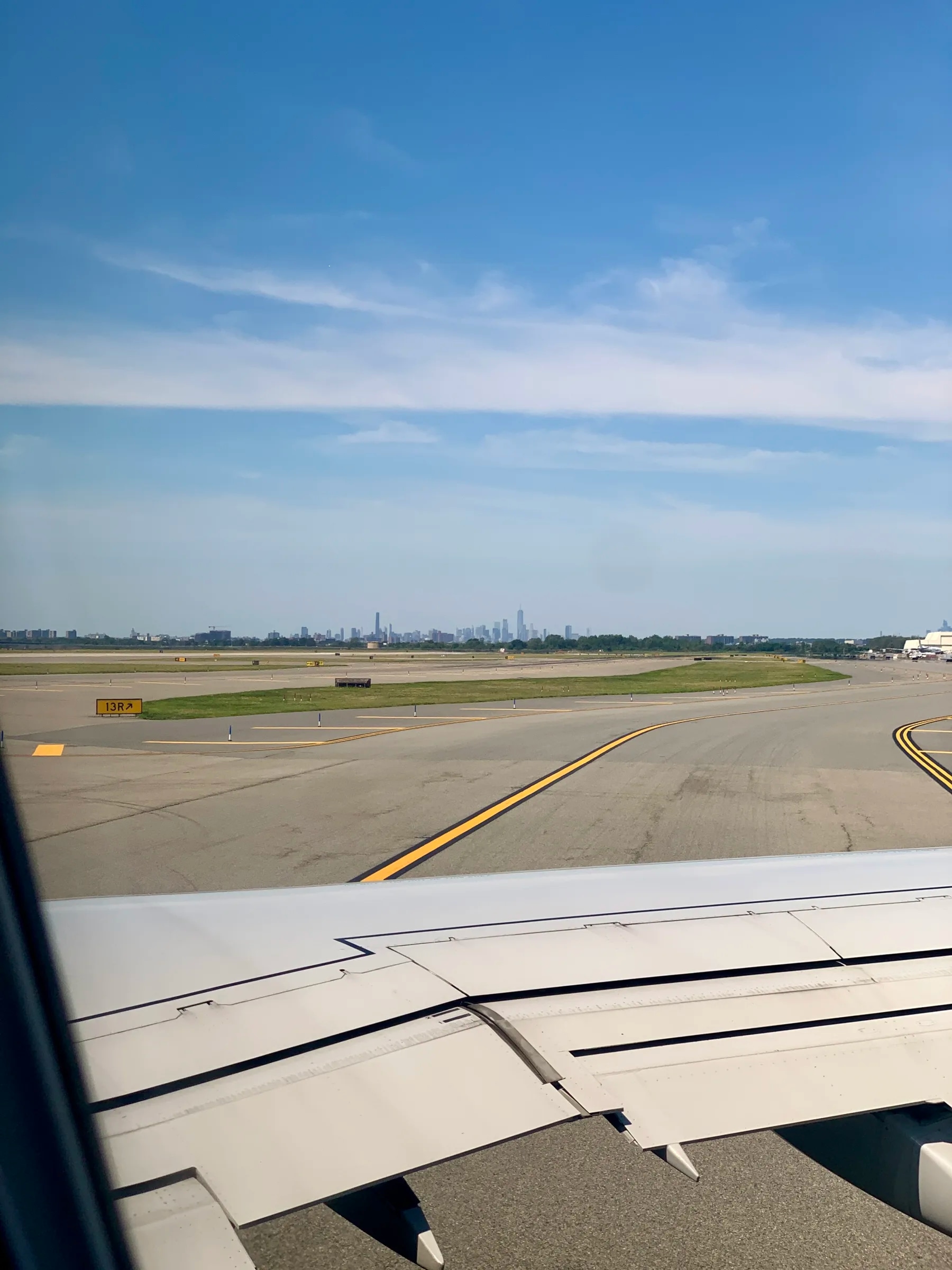 The Manhattan skyline in the distance beyond JFK's taxiways and the wing of an airplane.